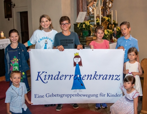 Eine Gruppe von Kindern in einer Kirche. Sie halten ein Banner mit der Aufschrift "Kinderrosenkranz - Eine Gebetsgruppenbewegung für Kinder".